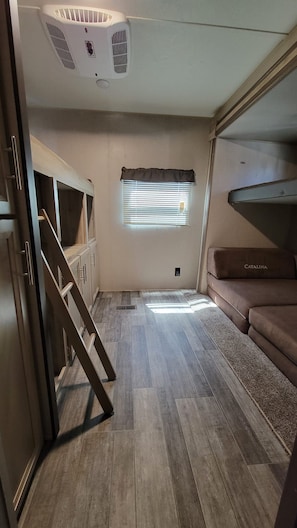 A compact RV interior with a kitchenette, a window with blinds, a sofa, and a ceiling fan. - Cozy 2-bedroom trailer with in wonderful Port Isabel. Indoor/outdoor pool & gym. (Port Isabel)