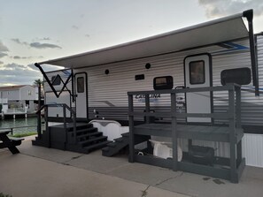 A recreational vehicle with a ramp leading to a covered area, a small table, and a bench. - Cozy 2-bedroom trailer with in wonderful Port Isabel. Indoor/outdoor pool & gym. (Port Isabel)