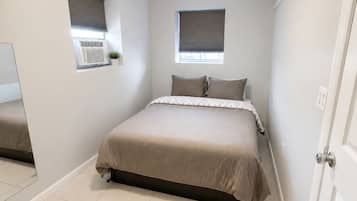 A bedroom with a bed, ceiling fan, windows, and an air conditioning unit.