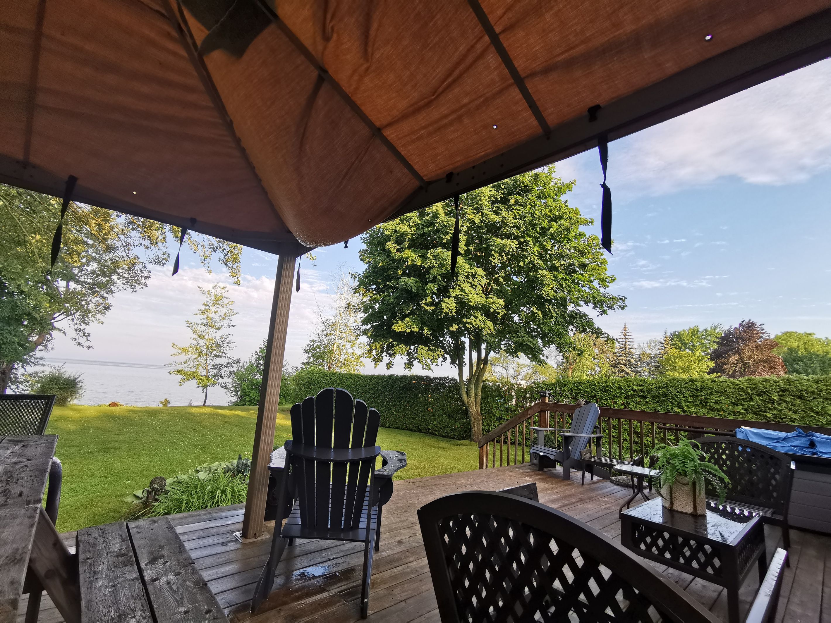 A covered outdoor deck with wooden furniture, a view of a lake, and a large tree.
