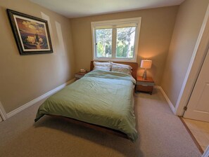 A bedroom with a bed, nightstands, a window, and a painting on the wall.