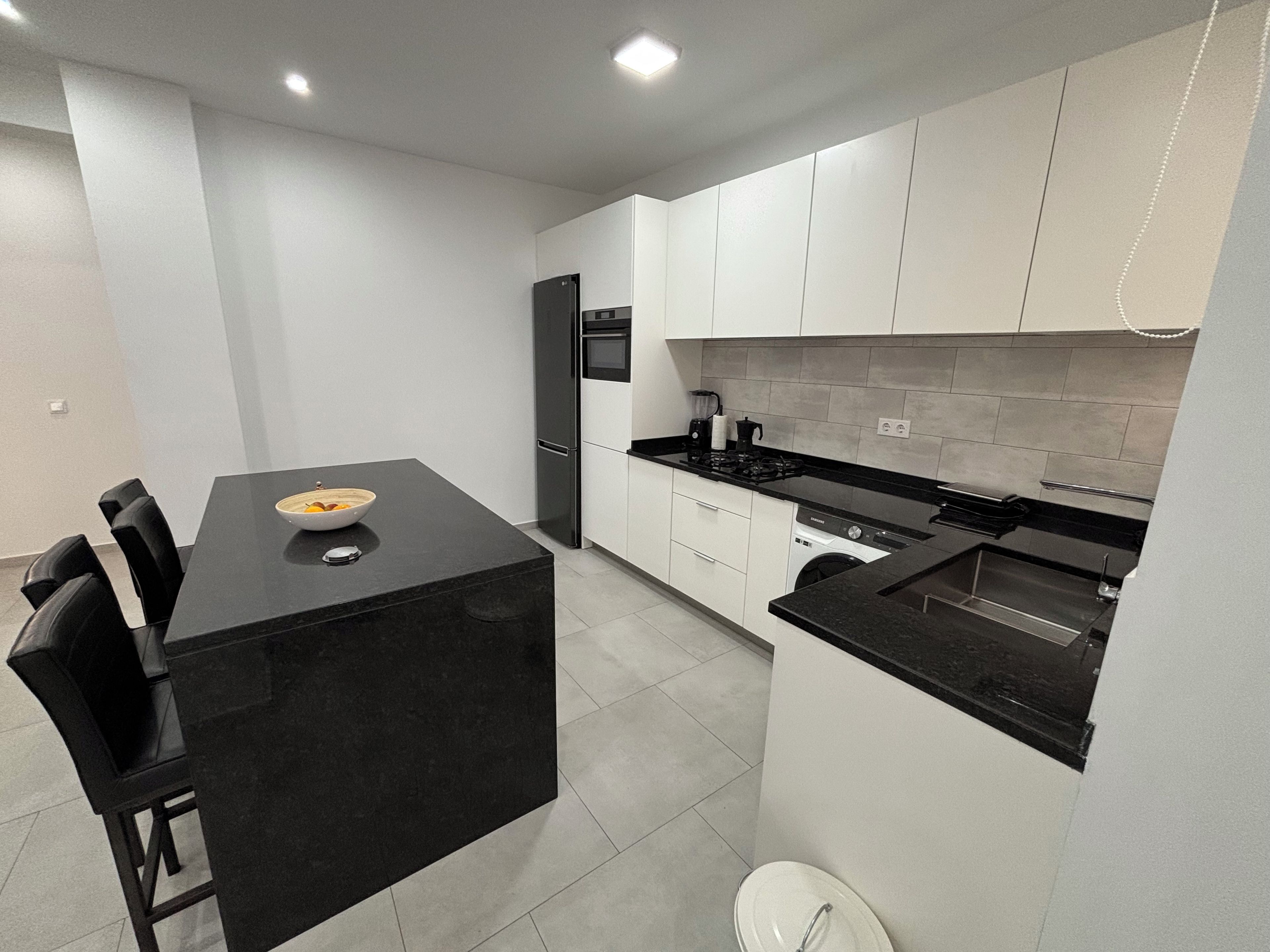 A modern kitchen with a black countertop, white cabinets, and a built-in dishwasher.