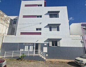 A multi-story residential building with a white facade and red accents, featuring a front entrance with a white railing and steps. - Spacious 2-Bedroom Apartment with Air Conditioning Near Laginha Beach (Mindelo)
