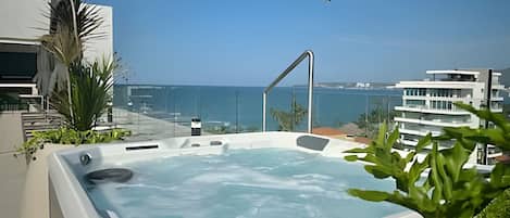 A hot tub with a view of the ocean and modern buildings.