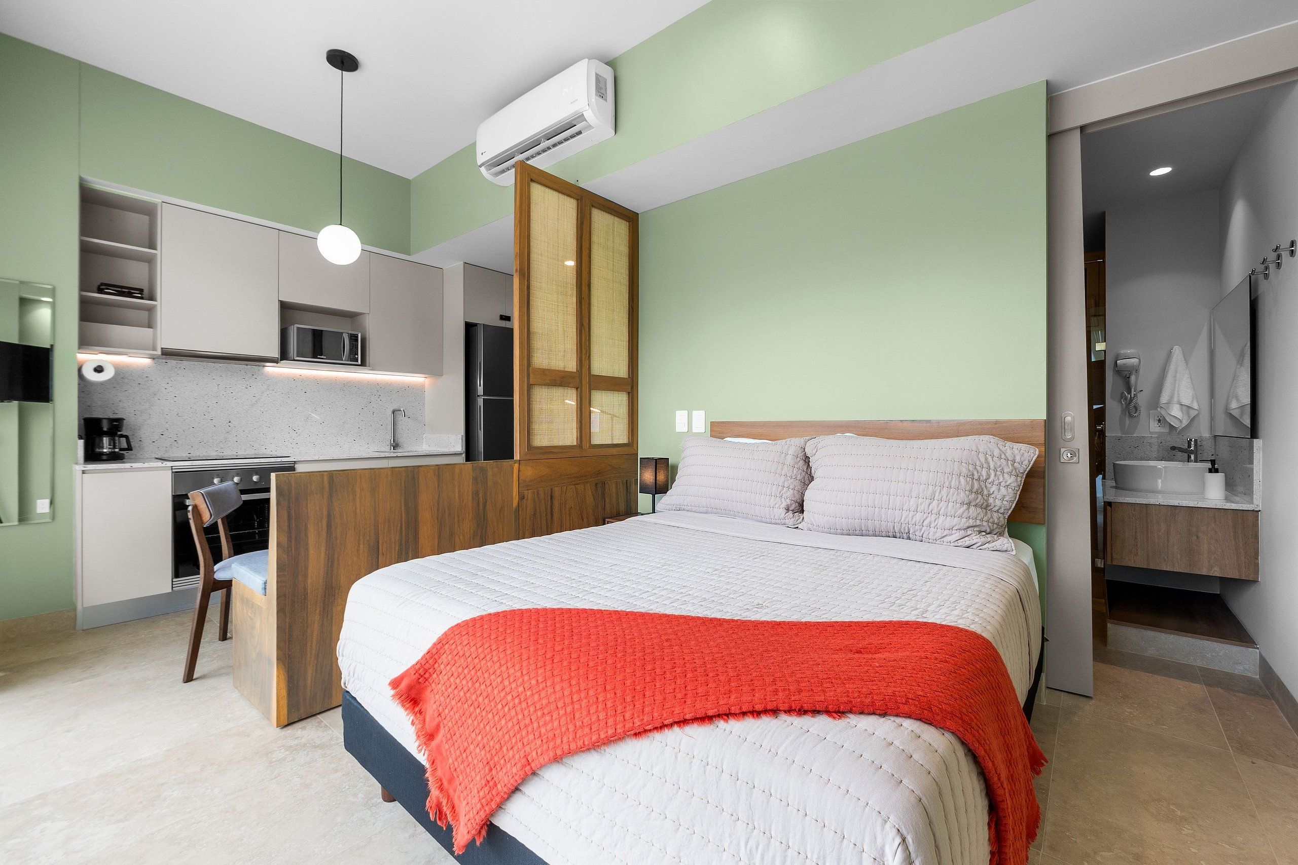 Ein modernes Schlafzimmer mit einem Bett, einer roten Decke, einem Holzkopfende und einer Küchenzeile im Hintergrund.