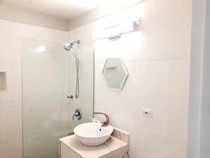 A modern bathroom with a glass shower enclosure, a white sink with a marble countertop, and a hexagonal mirror. - Cozy 1-bedroom apartment in fabulous Ocho Rios with AC (Ocho Rios)