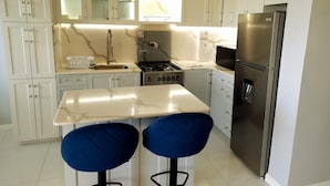 Una cocina moderna con armarios blancos, un refrigerador de acero inoxidable, una estufa a gas y dos taburetes azules.