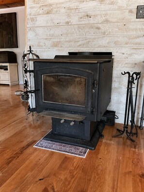 A wood-burning stove in a room with wooden flooring and a white brick wall.