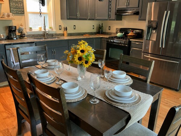 A kitchen with dark cabinets, stainless steel appliances, and a dining table set for six with white plates and glasses.