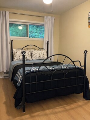 A single bed with a metal frame, a window with curtains, and a wall-mounted light fixture.