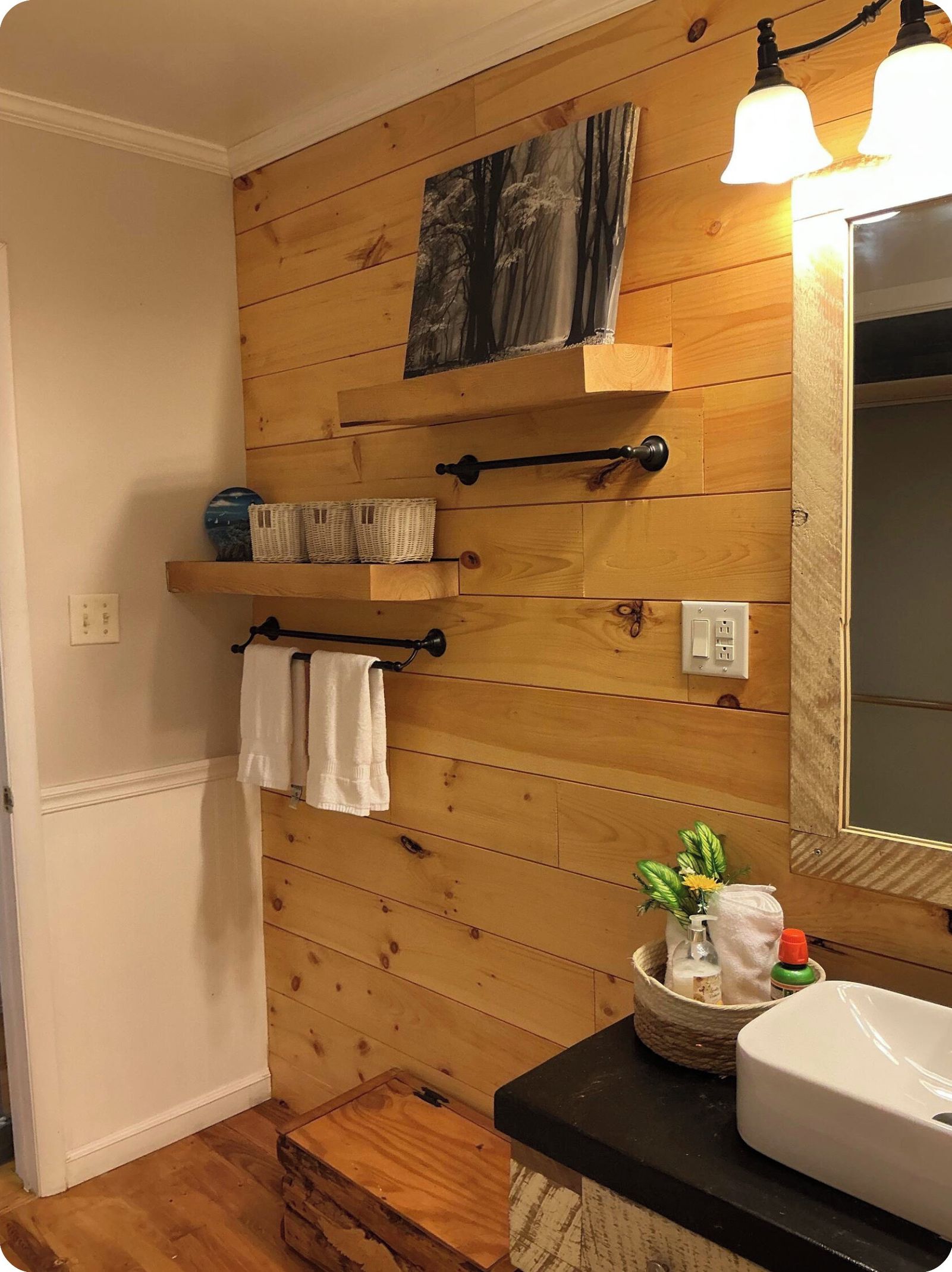 Une salle de bain avec des murs recouverts de panneaux en bois, un miroir, un lavabo et un porte-serviettes.