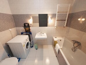 Ein kleines Badezimmer mit Waschmaschine, Waschbecken und Badewanne.