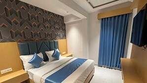 Une chambre d’hôtel moderne dotée d’un grand lit, d’une tête de lit ornée de motifs géométriques, d’un téléviseur à écran plat et d’une grande fenêtre avec des rideaux.