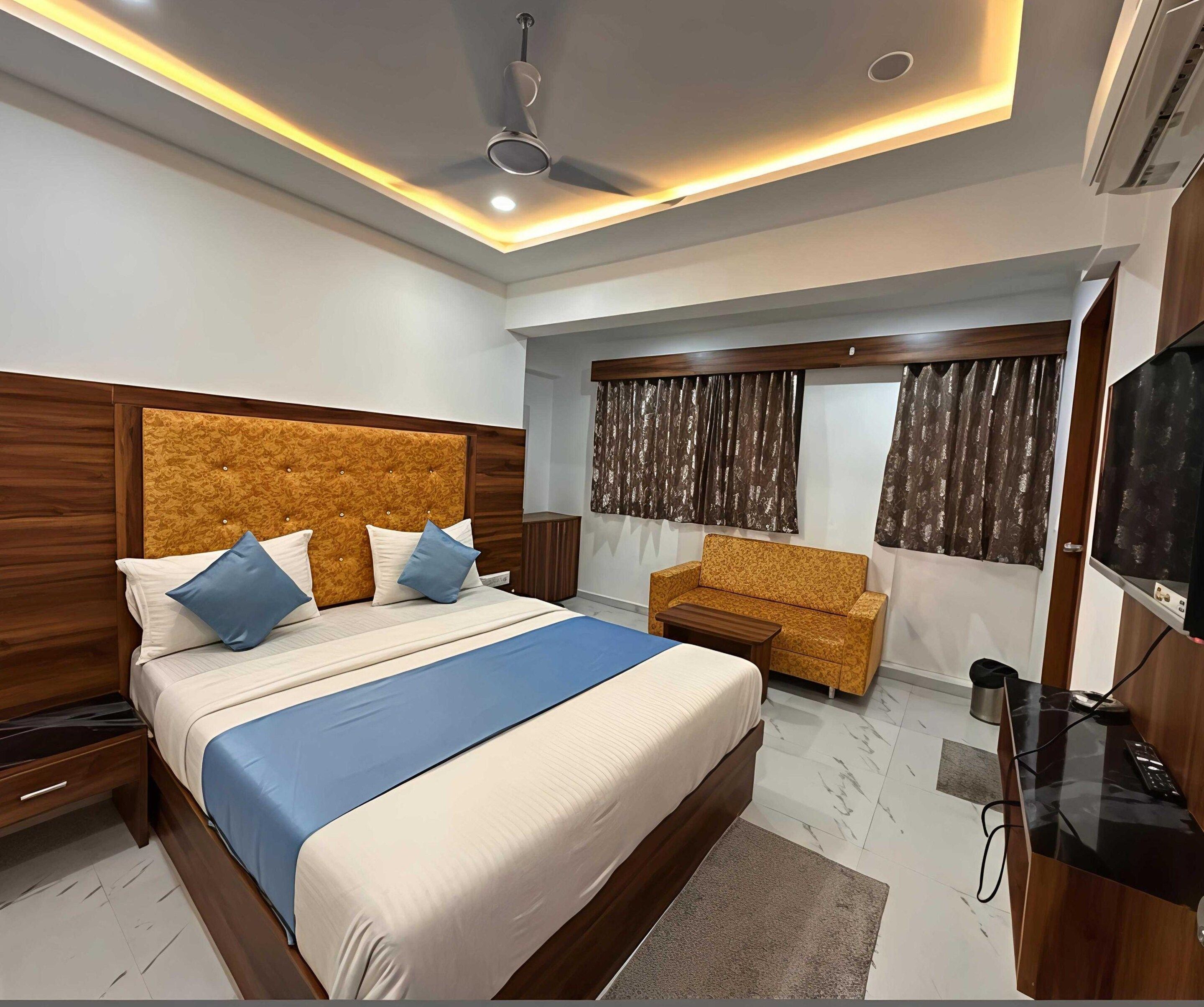A modern bedroom with a large bed, a sofa, a TV, and a ceiling fan.