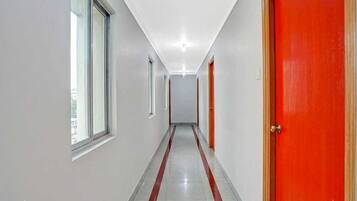 A corridor with a red door on the right, a window on the left, and a tiled floor.