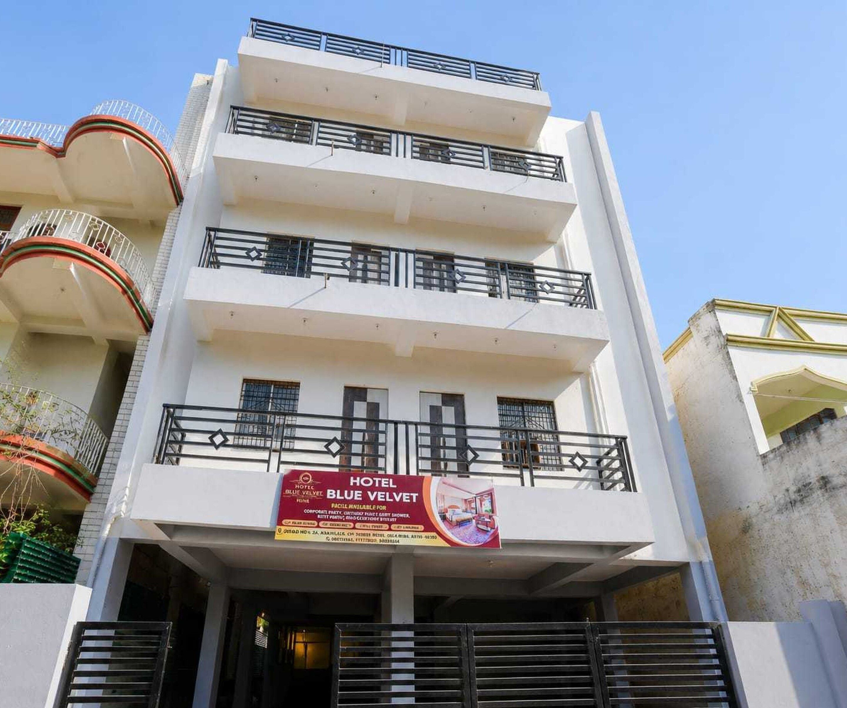 Un hôtel à plusieurs étages doté de balcons, une enseigne indiquant « HÔTEL BLUE VELVET », et une entrée fermée par un portail.