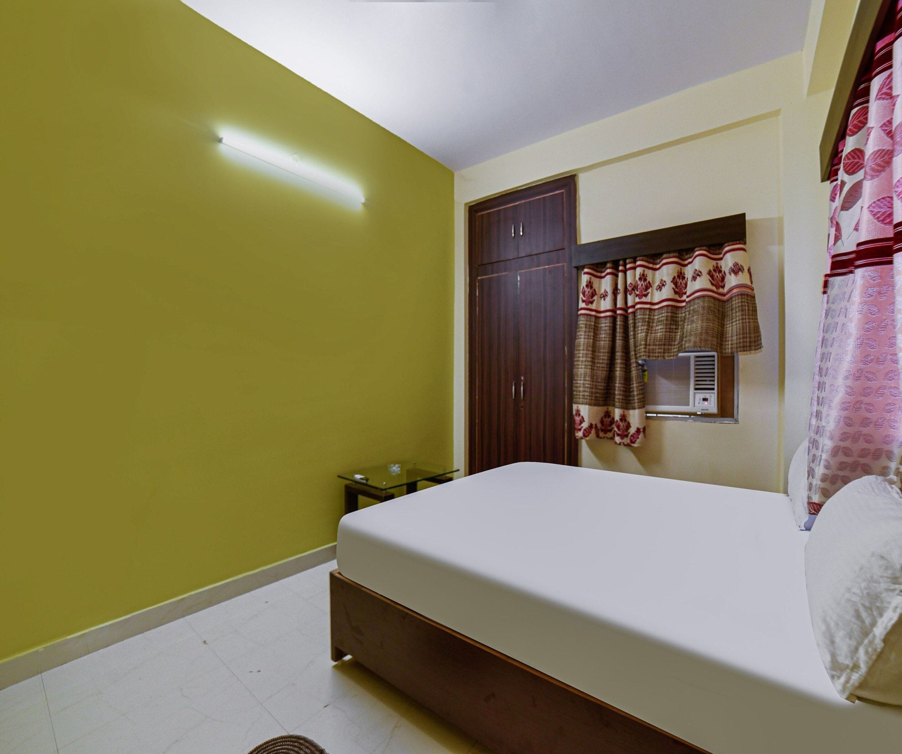 A bedroom with a bed, a wardrobe, a small table, and a window with curtains.