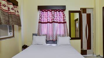 Une chambre d’hôtel avec un grand lit, une table de chevet, un téléphone et une fenêtre avec des rideaux à motifs.