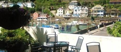 Un espace patio avec des sièges extérieurs et une vue sur une marina où sont amarrés des bateaux.