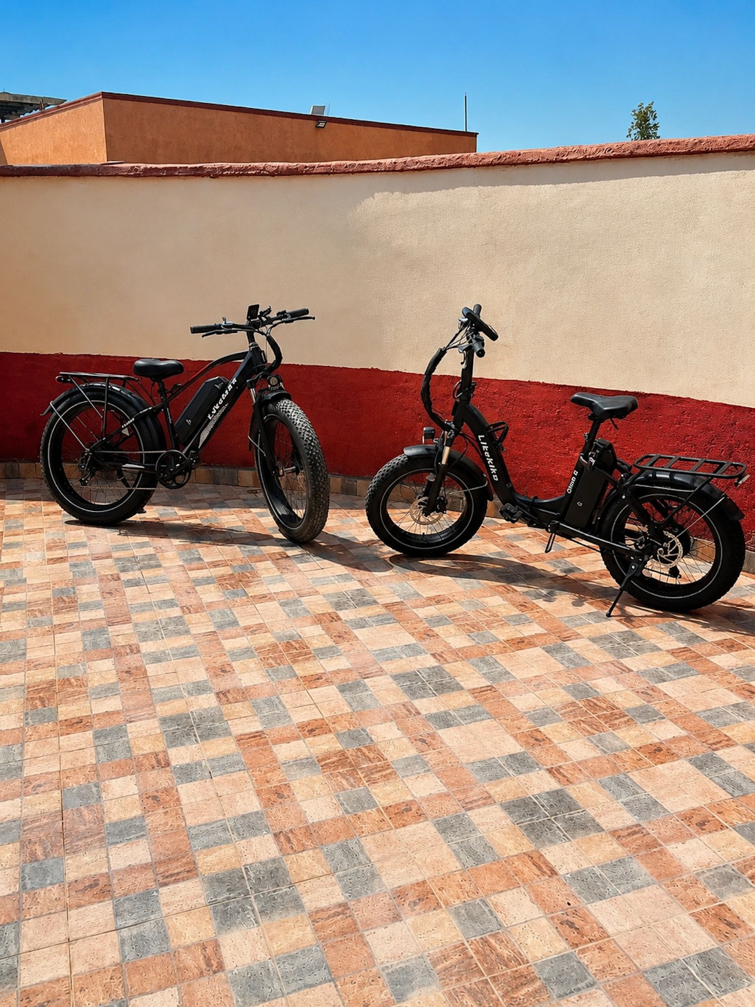 Two bicycles parked on a tiled patio with a red and beige wall in the background.
