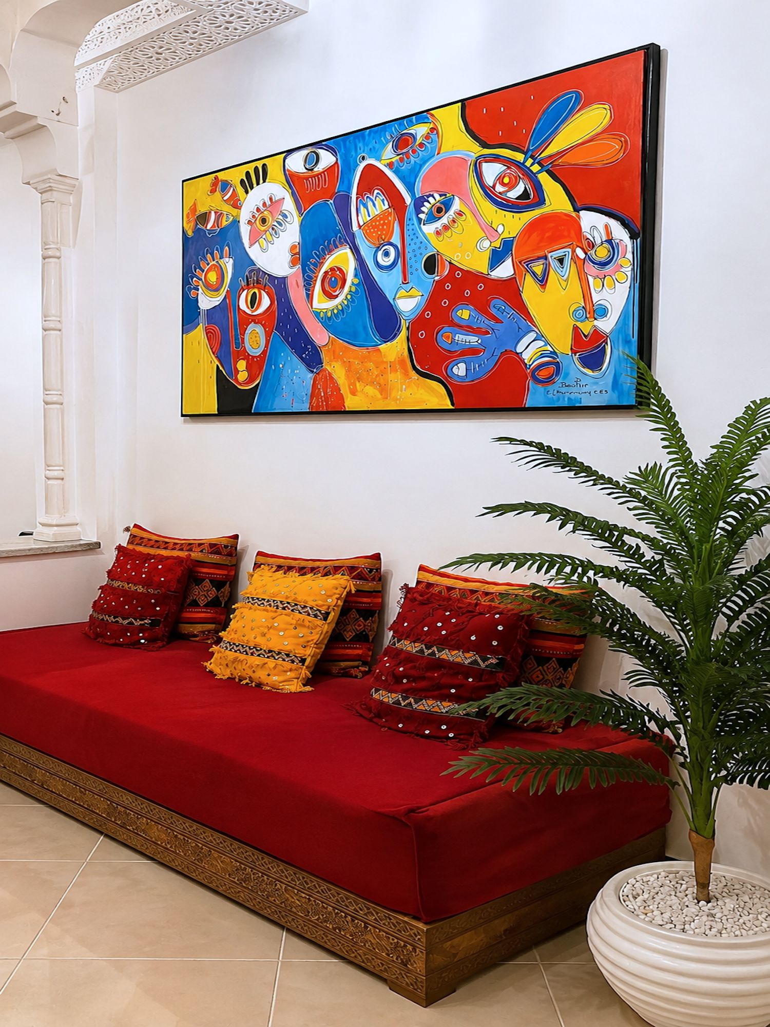 Un canapé rouge agrémenté de coussins à motifs, un grand tableau abstrait et une plante en pot, le tout dans un intérieur moderne.