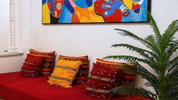 Un canapé rouge agrémenté de coussins à motifs, un grand tableau abstrait et une plante en pot, le tout dans un intérieur moderne.