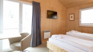 A room with a bed, a chair, a television, and a window with curtains. - Cabin in Turrach With Sauna and Wi-fi (Stadl-Predlitz)