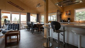 A modern kitchen with wooden beams, a bar area, and a seating area with chairs and a sofa. - Cabin in Turrach With Sauna and Wi-fi (Stadl-Predlitz)