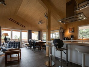 A modern kitchen with wooden beams, a bar area, and a seating area with chairs and a sofa. - Cabin in Turrach With Sauna and Wi-fi (Stadl-Predlitz)