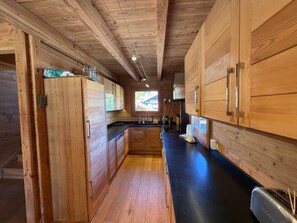 A wooden interior with a kitchen area, including cabinets, a countertop, and a window. - L'Evidence · Chalet luxe 10 pers · Sauna (Saint-Étienne-de-Tinée)