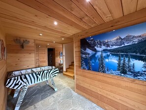 Interior em madeira com sofá estampado com padrão de zebra, cabeça de veado emoldurada e uma pintura mural paisagística.