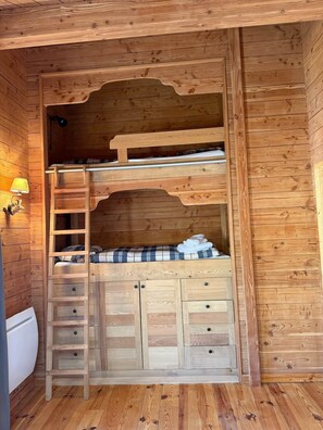 Uma cama beliche de madeira com escada, uma pequena escrivaninha e gavetas.