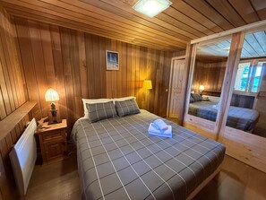 A wooden-paneled bedroom with a bed, bedside lamps, and a view through a door. - L'Evidence · Chalet luxe 10 pers · Sauna (Saint-Étienne-de-Tinée)