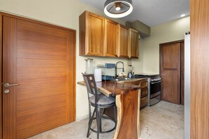 Une cuisine avec des meubles de rangement en bois, un tabouret de bar, un évier, une cuisinière et un luminaire au plafond.