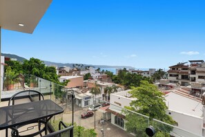 Ein Balkon mit Tisch und Stühlen, der auf eine Straße mit Gebäuden und einem klaren Himmel blickt.