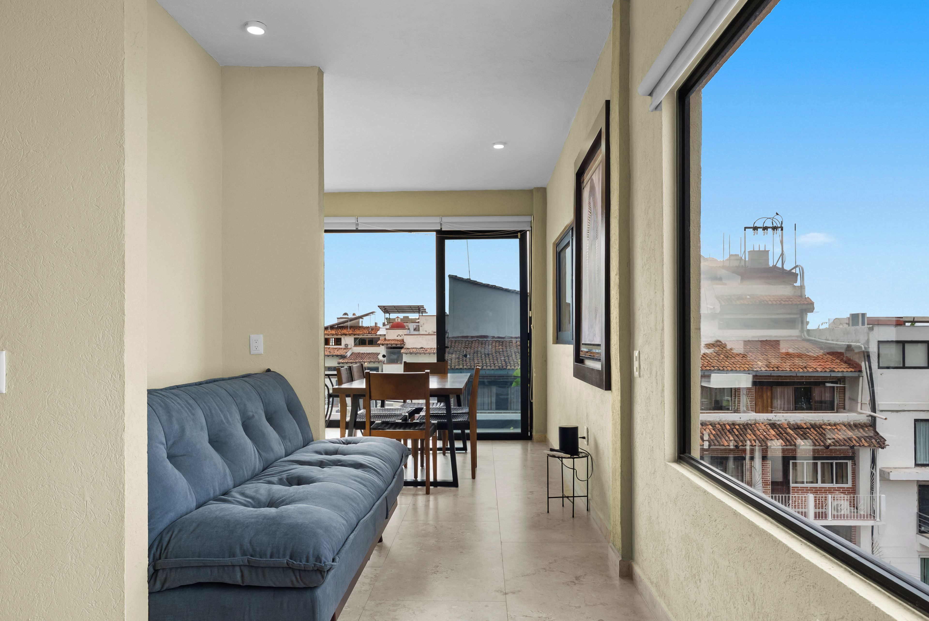Un balcón con sofá, mesa de comedor, sillas y vistas a edificios.