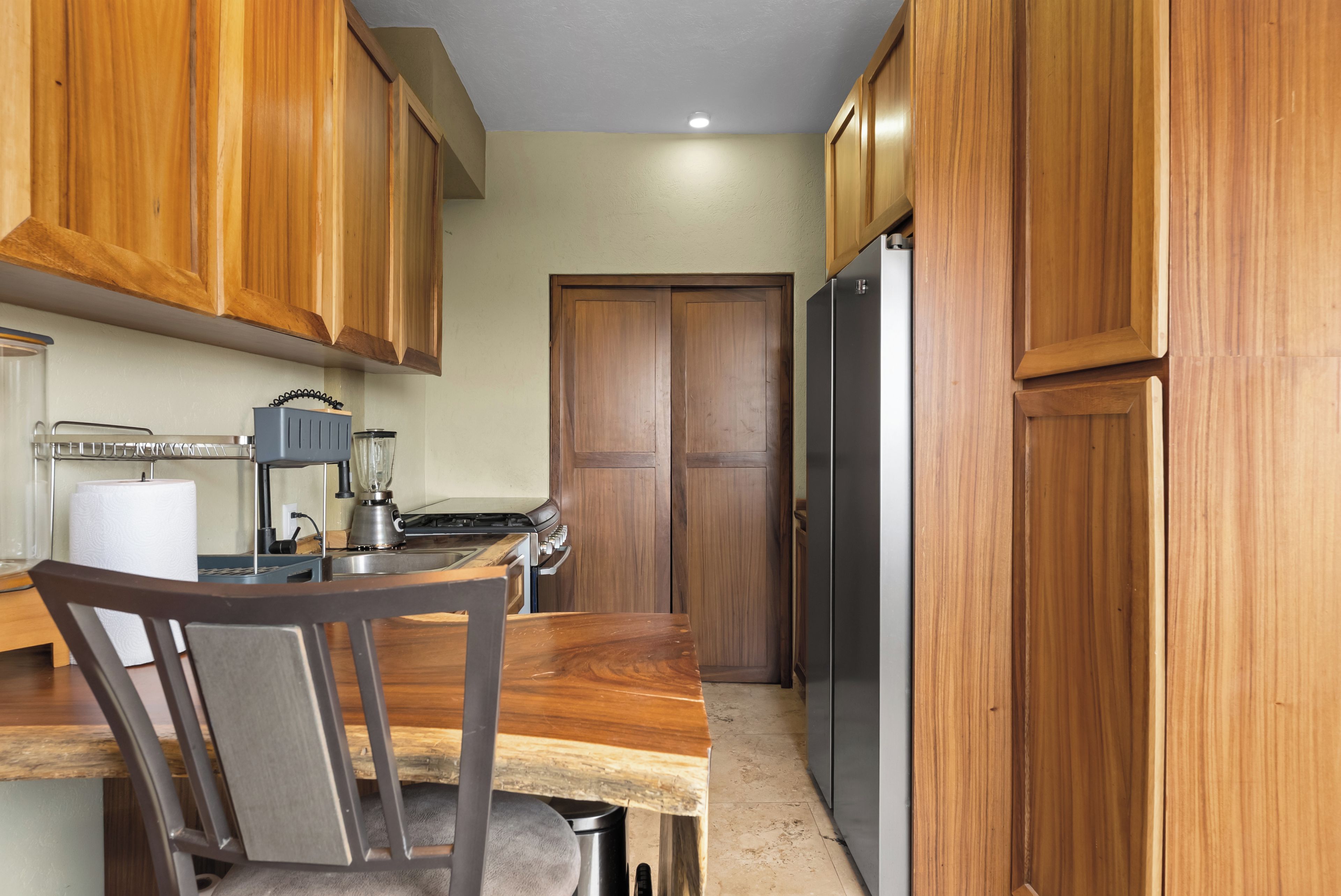 Una cocina con armarios de madera, un refrigerador, una estufa y una silla.