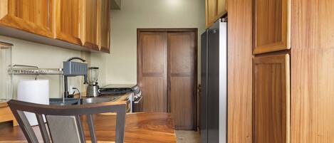 Una cocina con armarios de madera, un refrigerador, una estufa y una silla.