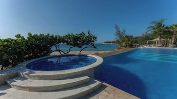 Une piscine d’un bleu éclatant, avec des marches permettant d’y descendre, entourée de palmiers et offrant une vue sur la mer.