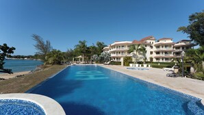 Resort com uma grande piscina, vista para a praia e edifícios de vários andares com varandas.