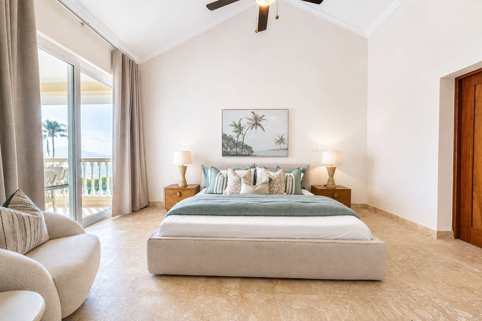 Une chambre avec un grand lit, deux tables de chevet avec des lampes, un ventilateur de plafond, une grande fenêtre avec des rideaux et un tableau encadré au mur.
