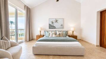 Une chambre avec un grand lit, deux tables de chevet avec des lampes, un ventilateur de plafond, une grande fenêtre avec des rideaux et un tableau encadré au mur.