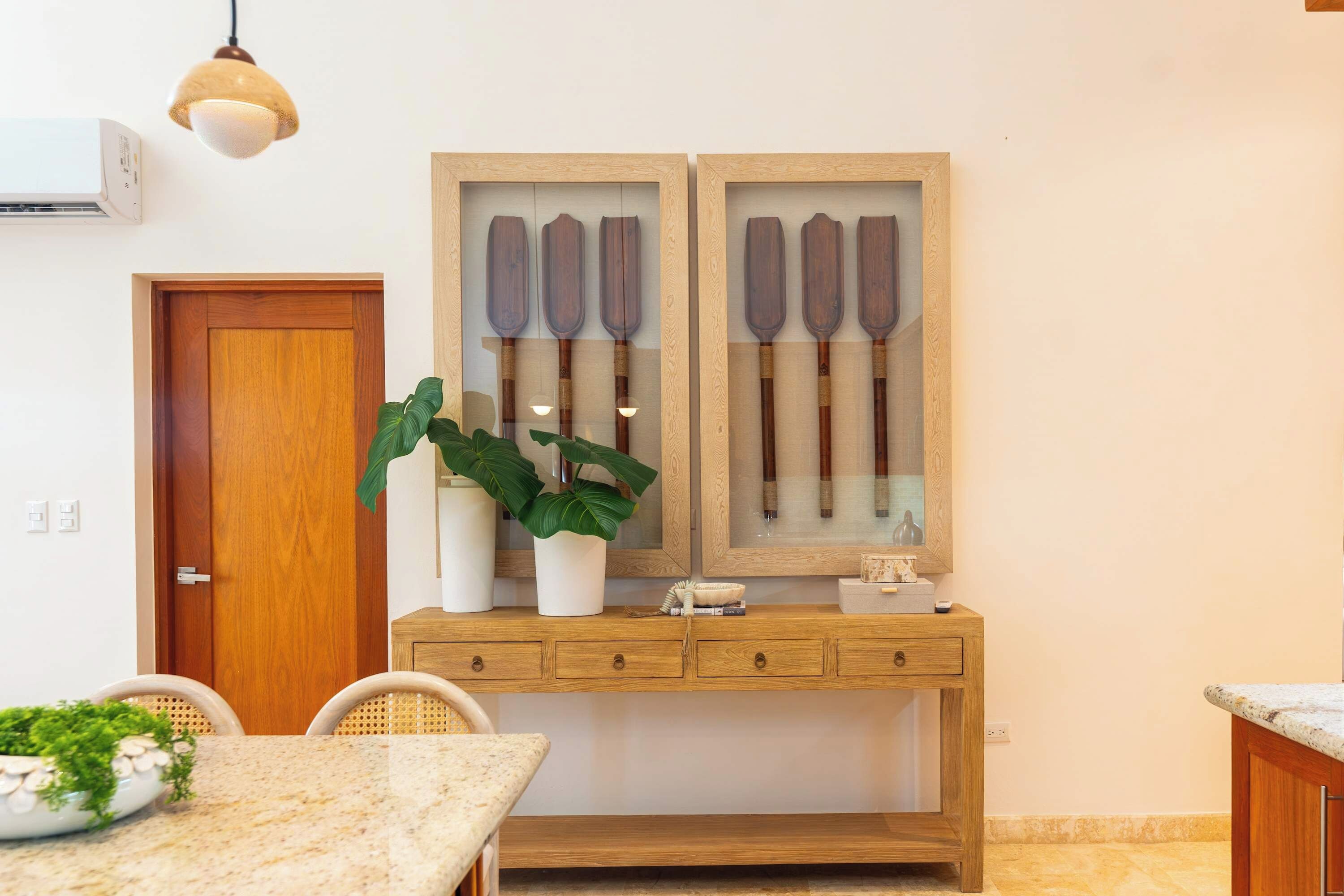 Un comedor con un armario de madera, dos plantas en macetas y un exhibidor de palas en la pared.