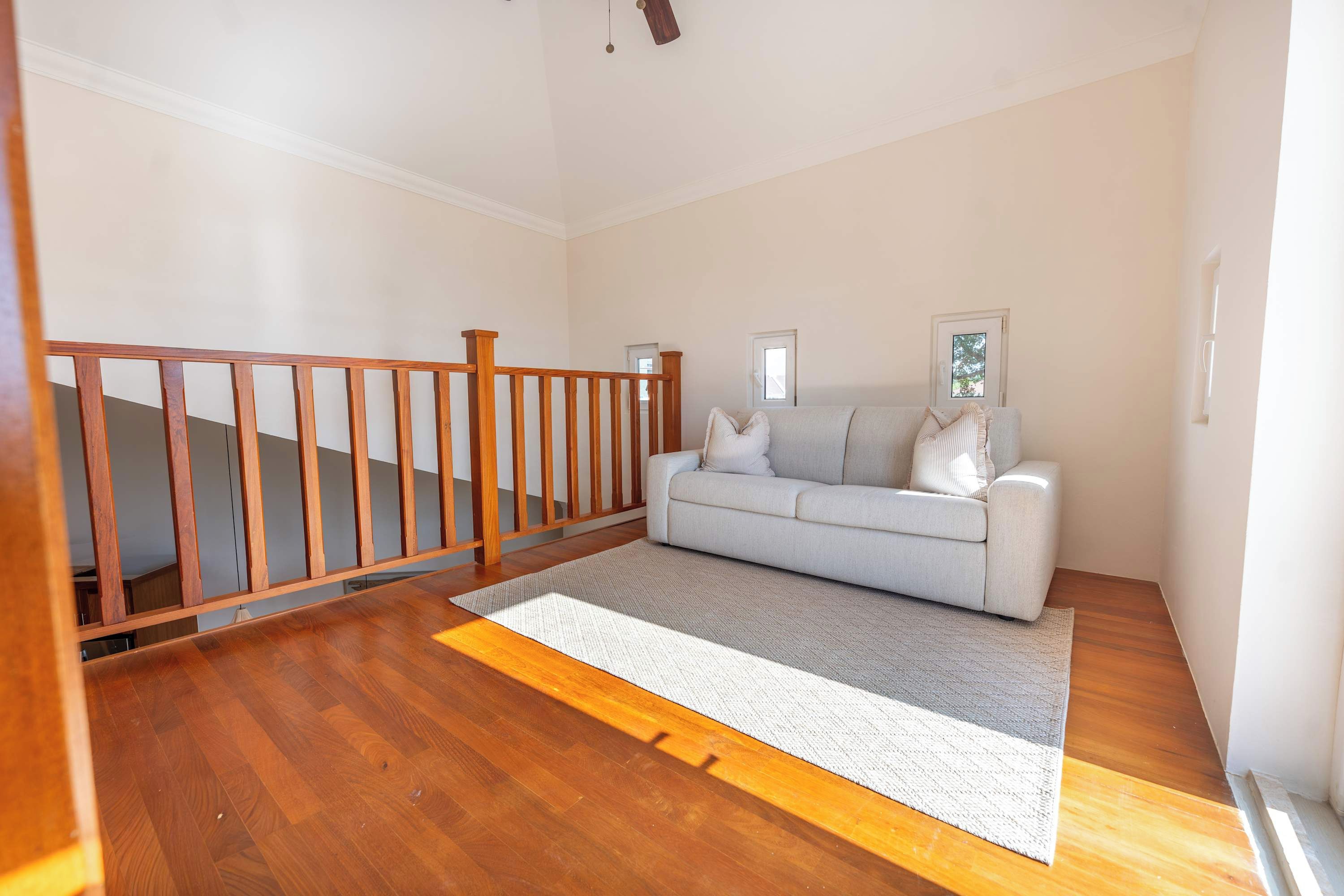 Une pièce avec un escalier en bois, un canapé gris et un tapis à motifs.