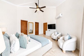 A modern bedroom with a bed, a sofa, a TV, and a ceiling fan. - Luxury Beachfront Apartment in Sosua! (Sosúa)