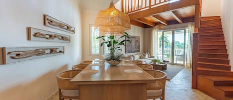 A spacious dining area with a long wooden table, wicker chairs, and a hanging light fixture.