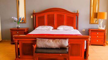 Un dormitorio con una cama grande, cabecera de madera, dos mesitas de noche, un banco y dos espejos montados en la pared.