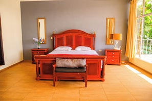 Une chambre à coucher avec un grand lit, deux tables de chevet, un banc et une fenêtre avec des rideaux.