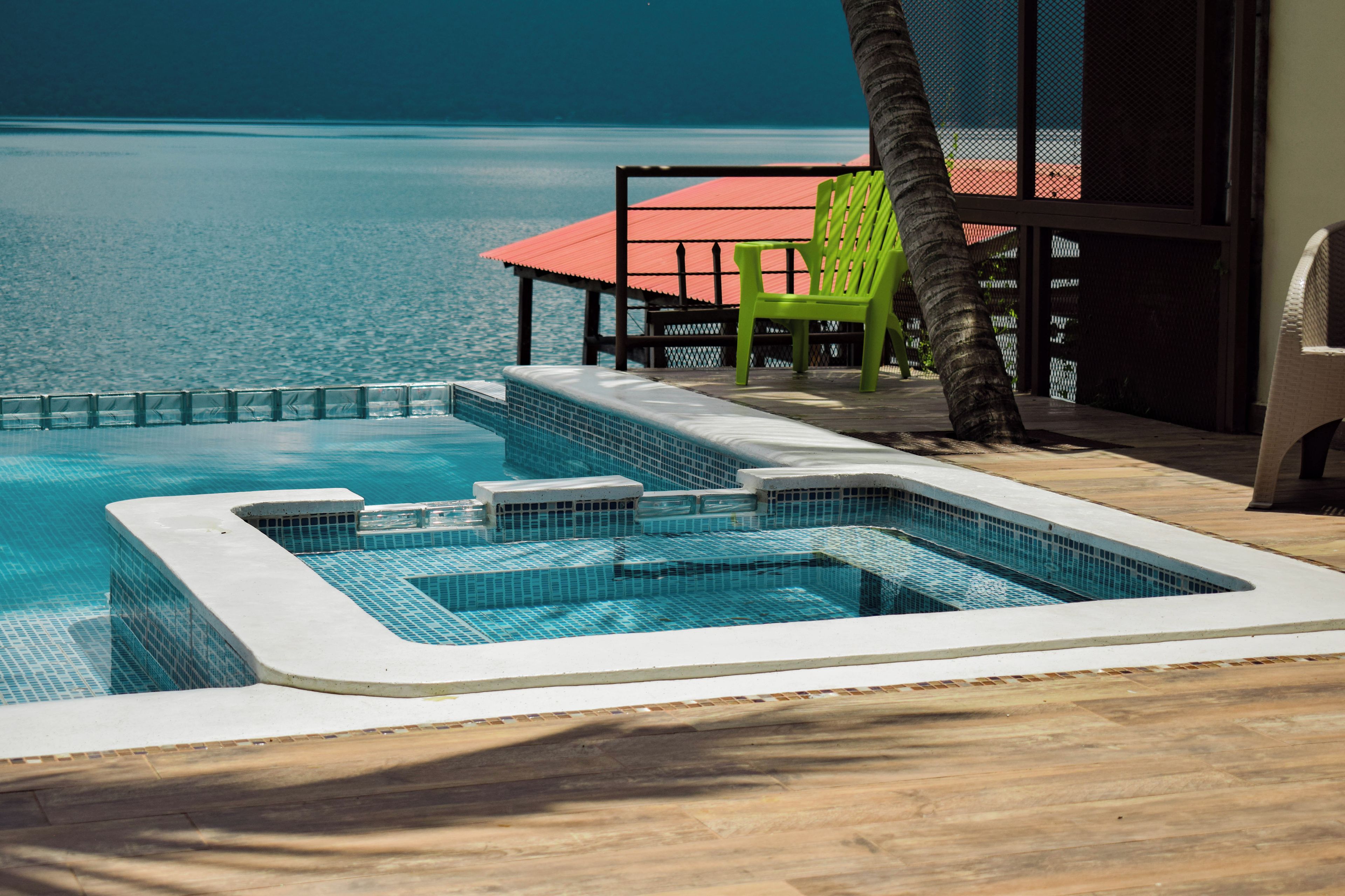 A swimming pool with a tiled edge, a lounge area with a red roof, and a green chair.