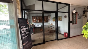 Una habitación con puerta de vidrio corrediza que da a una zona de cocina, un cartel negro con texto, un reloj en la pared y una planta en maceta.